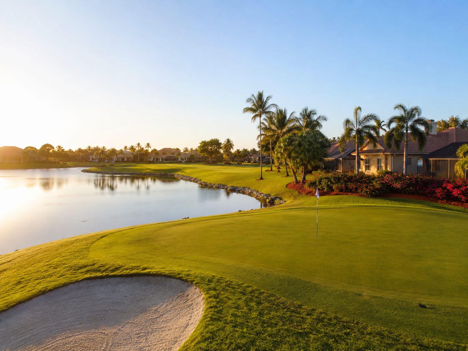 A golf fairway curving around open water, palms and homes beyond
